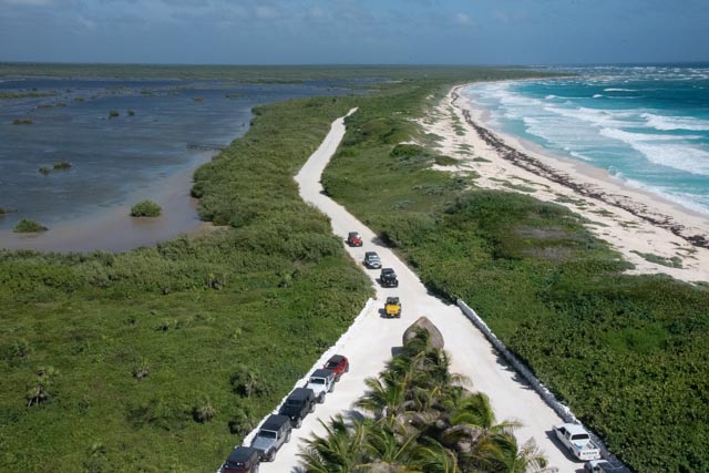 A caravan of Jeeps in a paved road with a lagoon in onside and the Sea on the other